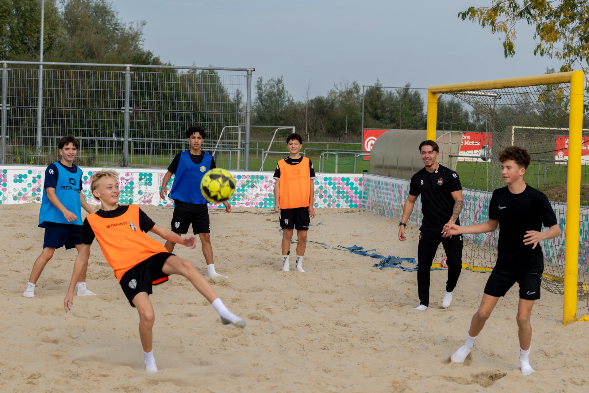 Trainer Danny Hoefnagels speelt een voetbalpartij met kinderen op het zandveld