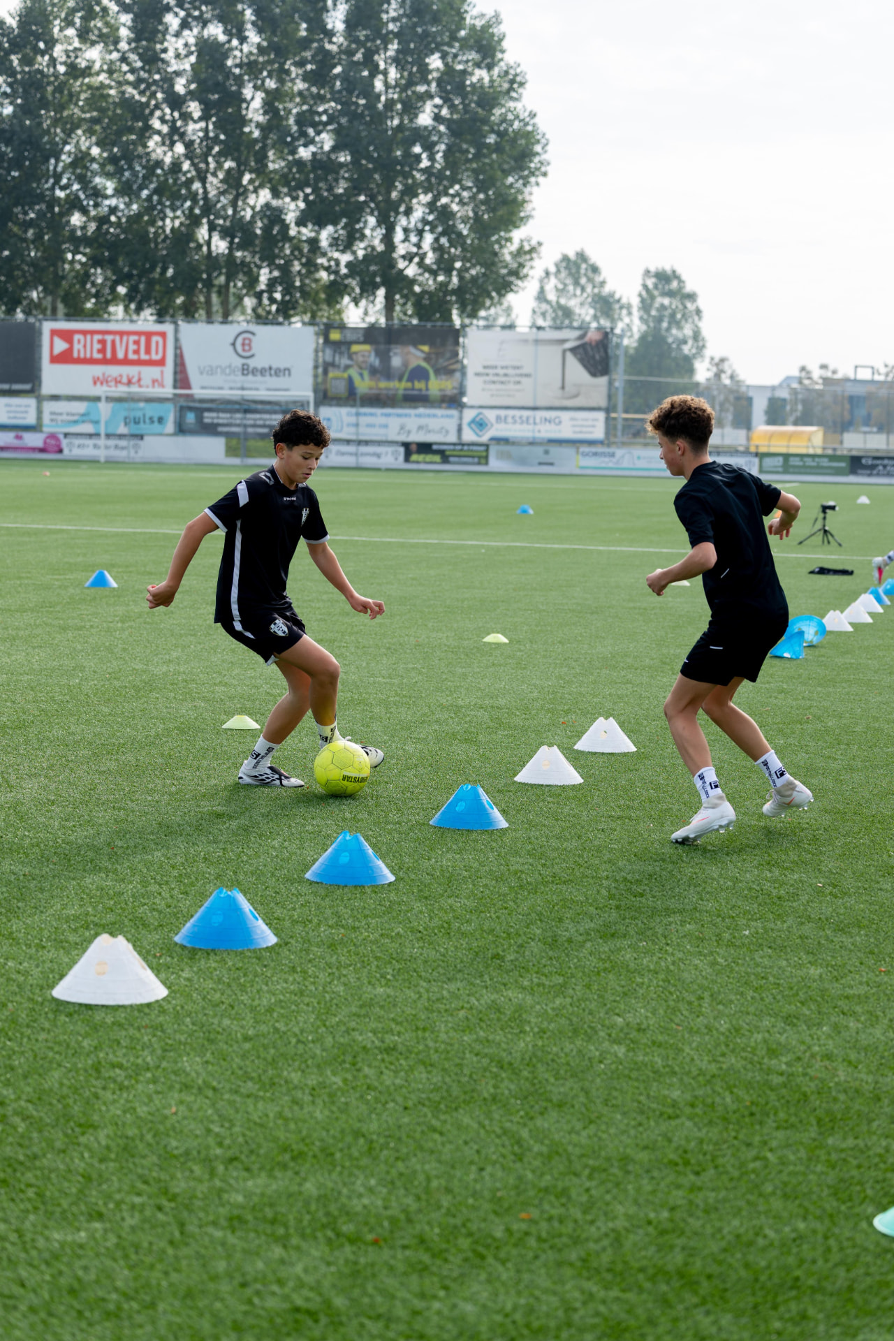 Twee kinderen dribbelen in een slalom tussen pionnen tijdens de training